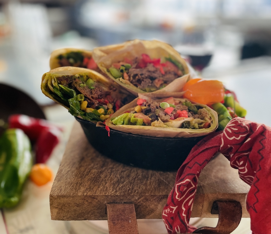 Freshly prepared burritos with vibrant fillings served on a wooden board next to a glass of red wine and peppers.