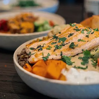 Grilled salmon bowl topped with fresh herbs, served with lentils, roasted sweet potatoes, hummus, and vegetables at Feta Cowboy.