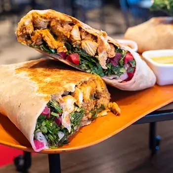 Grilled chicken shawarma wrap stuffed with fresh greens, pickled vegetables, and herbs, served with dipping sauce at Feta Cowboy.